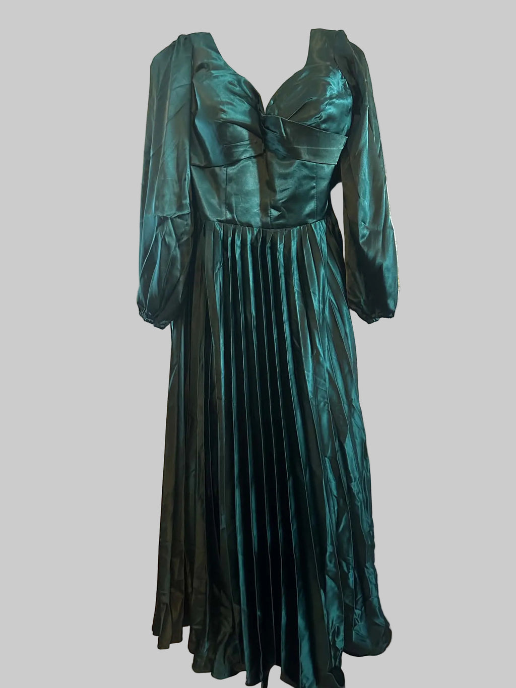 A floor-length emerald green satin gown with long balloon sleeves, a sweetheart neckline, and a pleated skirt, hanging against a vintage floral wallpaper background.